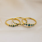 The Lace Birthstone Rings Set features three delicate rings with small blue gemstones, displayed on soft beige fabric—a perfect personalized gift for lovers of minimalist jewelry.