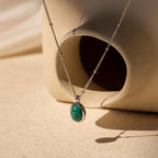 The Turquoise Pendant Necklace, featuring a silver boho-chic design with an oval turquoise pendant, is draped over a cream abstract ceramic vase.