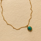 The Turquoise Pendant Necklace features a gold chain and an oval turquoise pendant, styled on a beige textured background for a subtle boho-chic vibe.
