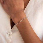 Close-up of a delicate Multiple Baguette Birthstone Bracelet with a small red gemstone, elegantly layered over a white shirt on a person's wrist.