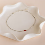 The Multiple Baguette Birthstone Bracelet, featuring sparkling birthstones, is displayed on a wavy white ceramic dish.