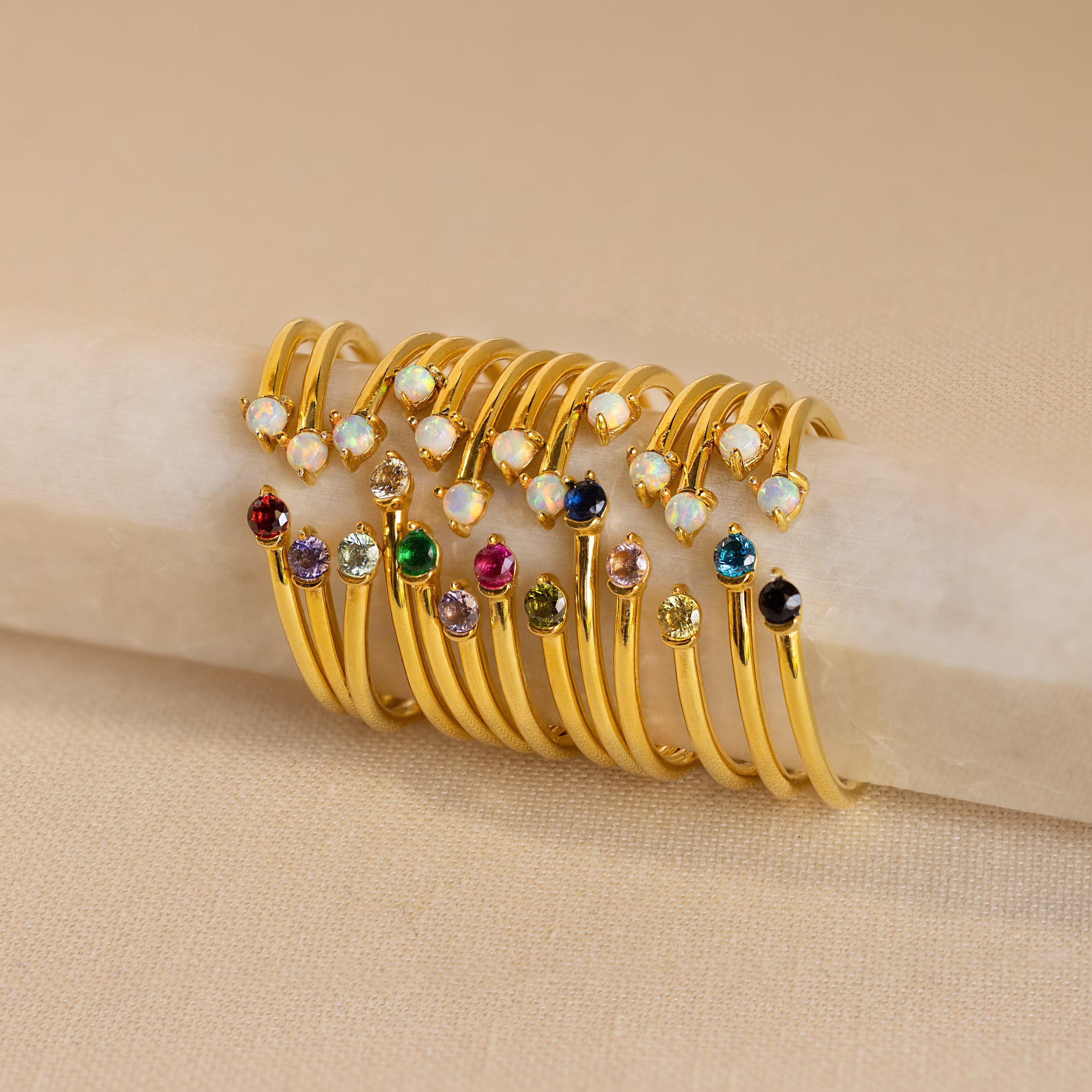 The Duo Birthstone & Opal Ring, featuring colorful gemstones, is displayed in a row on a light beige surface.