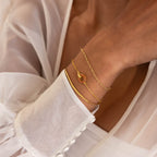 A woman wears gold bracelets, including the Interlocking Birthstone Bracelet, a beautiful customizable piece, and a sheer white blouse with buttoned cuffs.