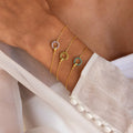 A hand wears three Interlocking Birthstone Bracelets—gold chains with circular gemstone charms—resting on white fabric. This stunning birthstone jewelry is perfect for stacking or gifting.