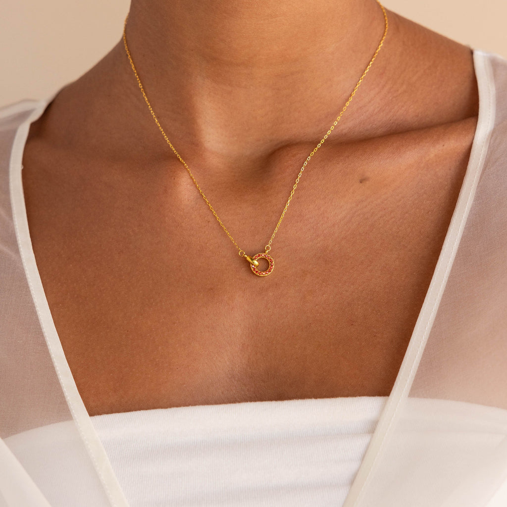 The Interlocking Birthstone Necklace features a circular pendant, worn on the neck and styled with a white top—an elegant keepsake gift for mom.