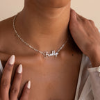 A woman wears the Luna Name Necklace in Paperclip Chain, a silver personalized necklace with "Brooklyn" in cursive above her collarbone.