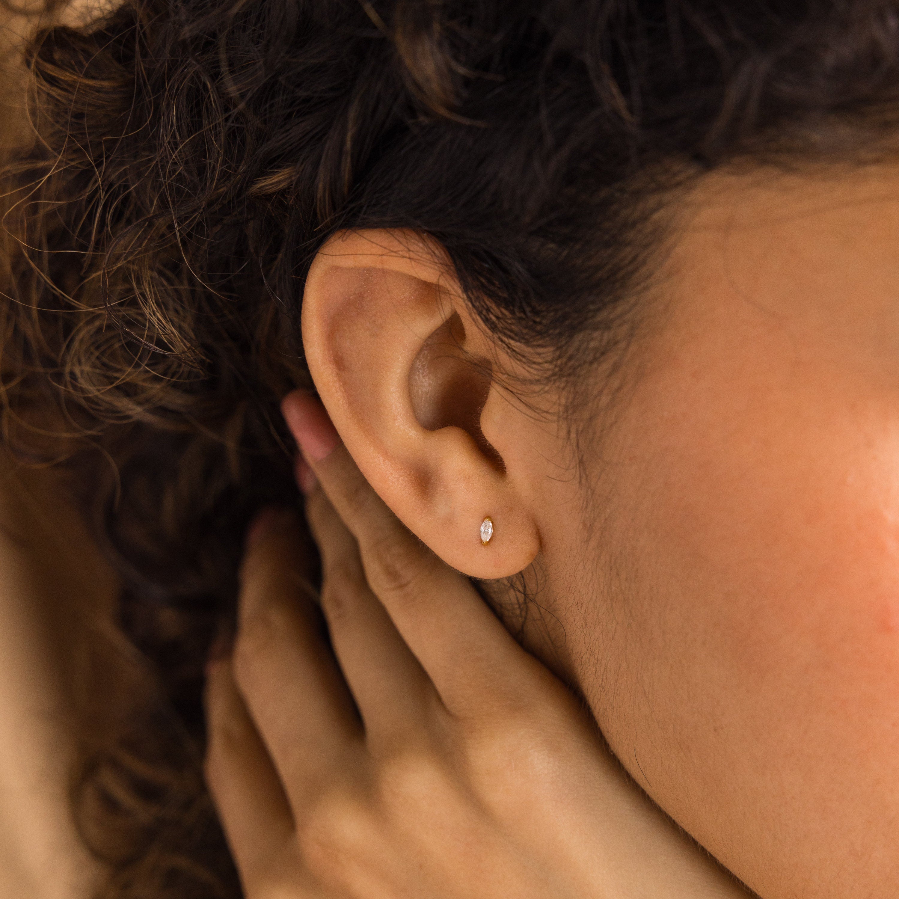 A close-up of a woman's ear wearing Marquise Birthstone Studs, her hand softly touching her neck, showcasing the elegance of personalized gemstones.