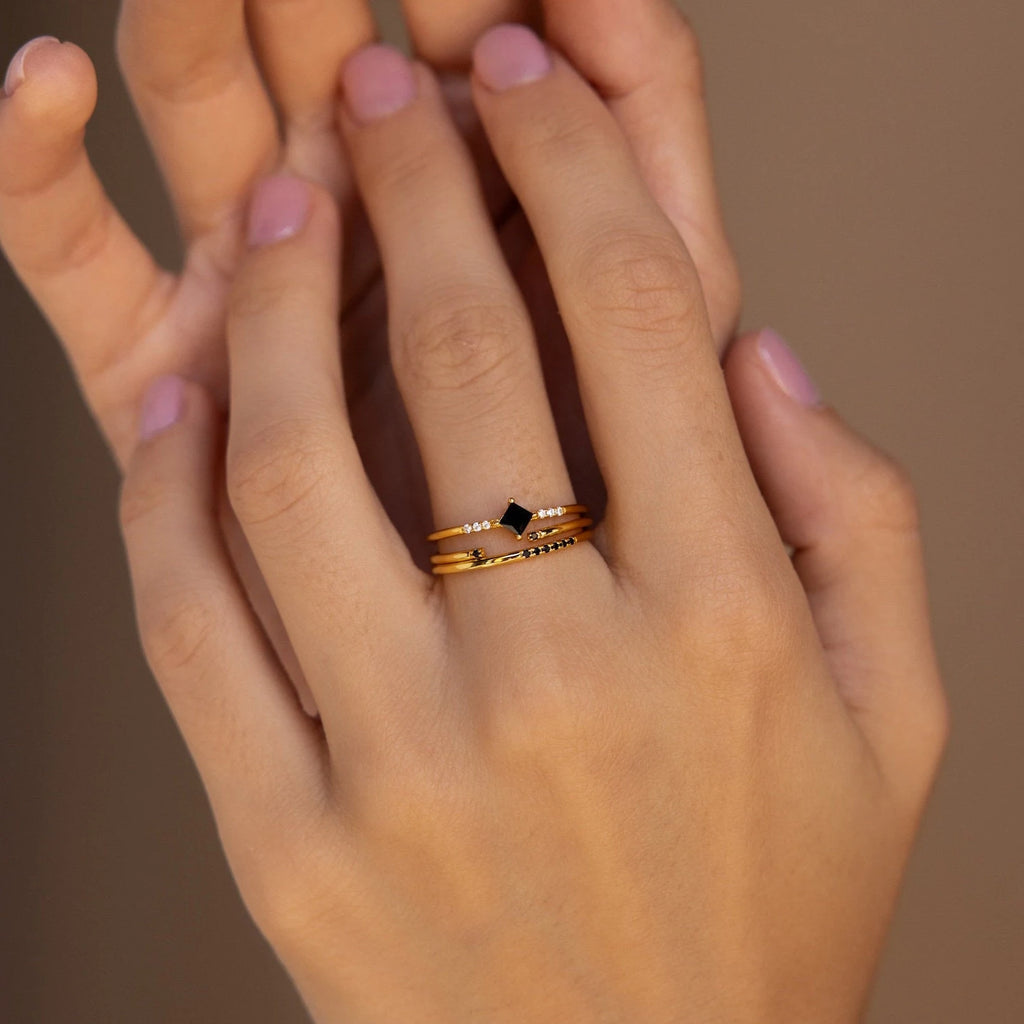 A hand with light pink nails wears three stacked gold rings from the Black Diamond Rings Set, creating a chic layered jewelry look.