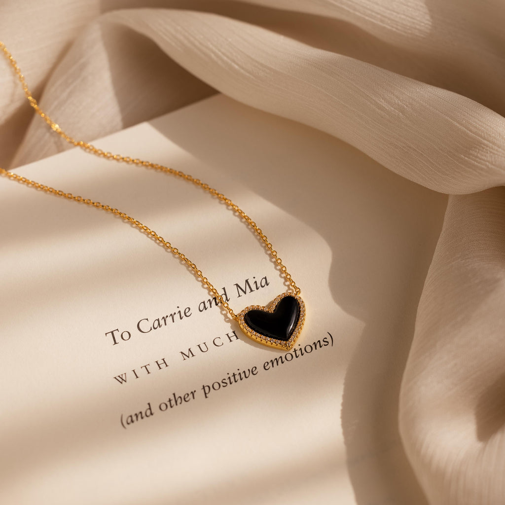 The Pave Onyx Puff Heart Necklace in 18K Gold features an onyx heart pendant and is displayed atop a page printed with a heartfelt message.