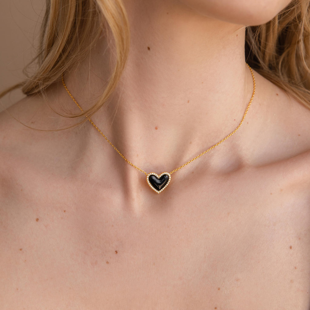 A woman embodies coquette style wearing the Pave Onyx Puff Heart Necklace, its gold chain and black heart pendant resting elegantly against her skin.