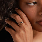 A person with curly hair wears layered gold rings, including the Black Diamond Rings Set adorned with dark stones and delicate details, on their finger.