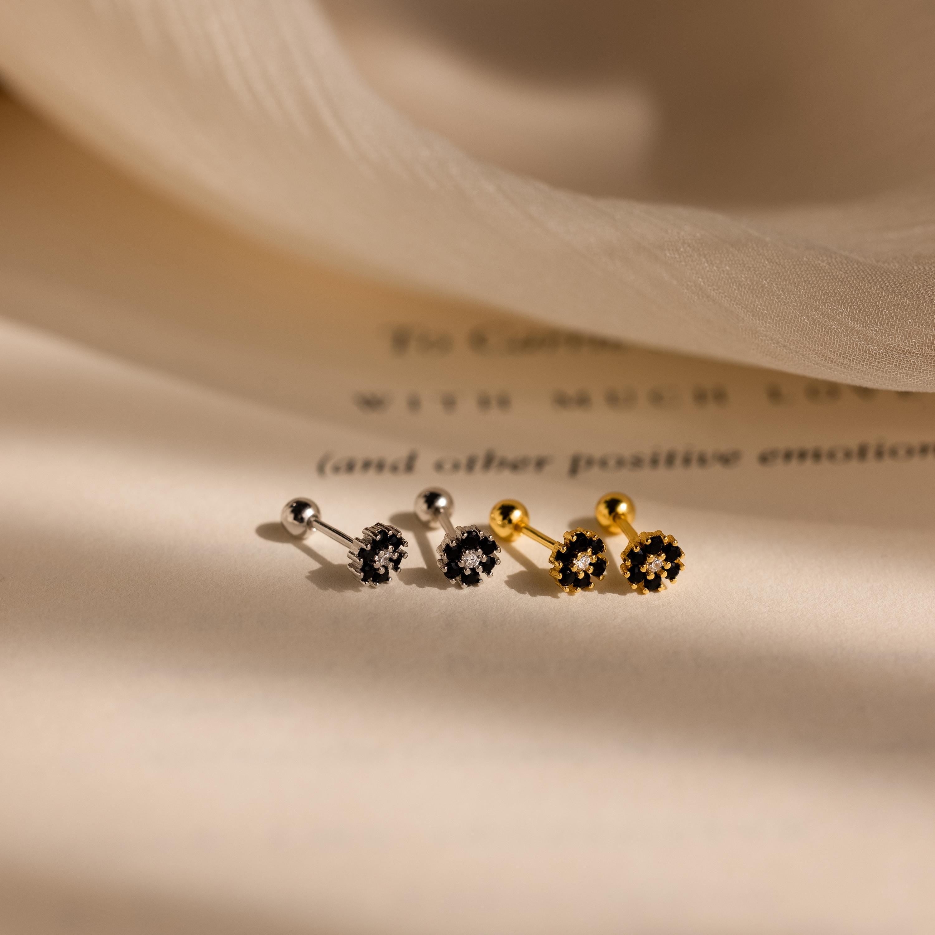 The Onyx Flower Studs, along with another pair of silver and gold stud earrings featuring black onyx stones, are elegantly displayed on a soft beige surface.
