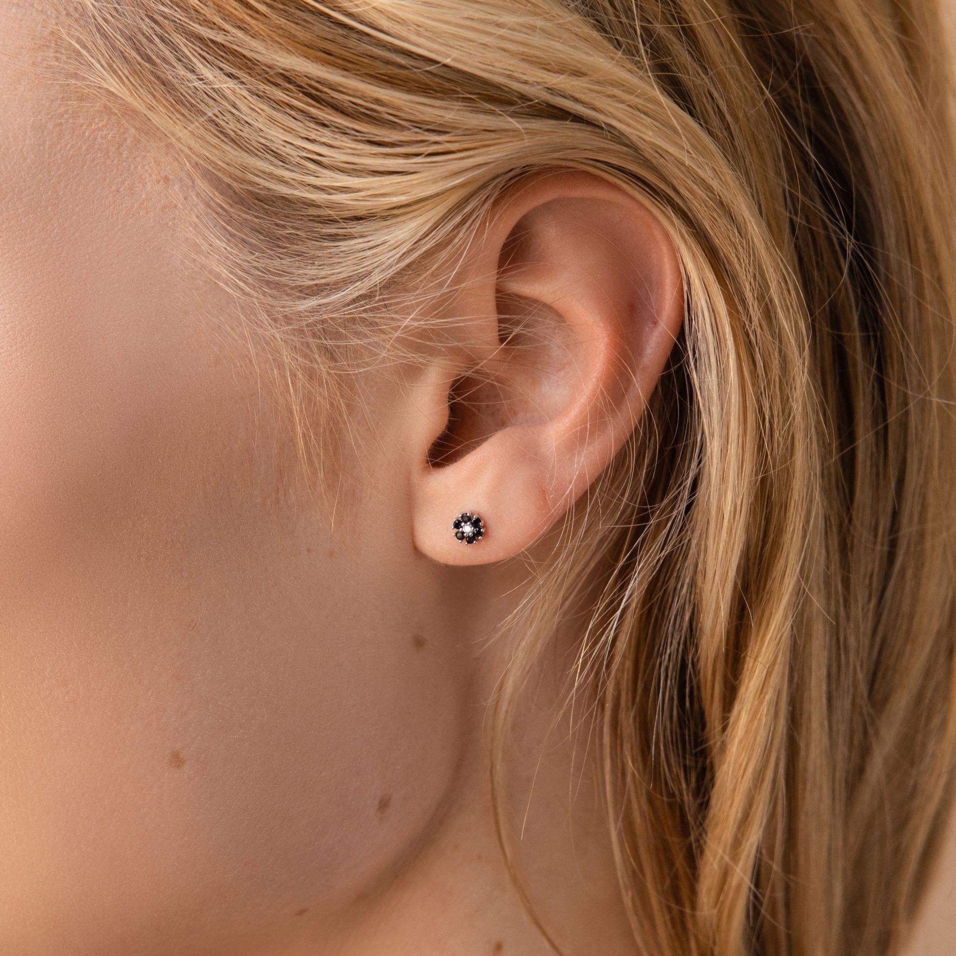 Close-up of a woman's ear wearing Onyx Flower Studs with a floral design, her blonde hair beside the flatback earrings.