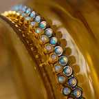 The Opal Bezel Tennis Necklace, featuring iridescent opal stones set in gold, is displayed on a reflective golden-yellow surface, radiating timeless elegance.