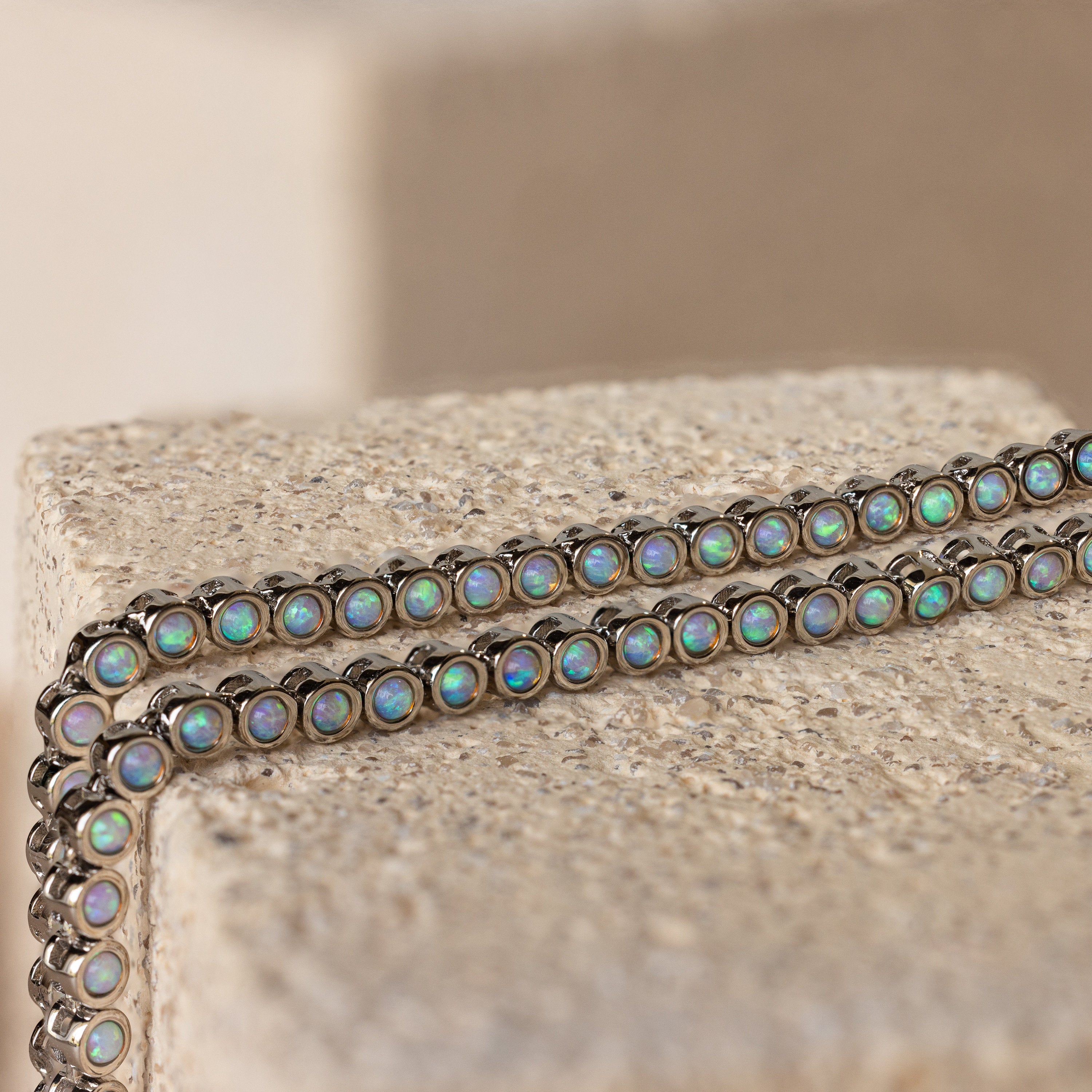 A silver chain bracelet with round iridescent opal stones, draped over a textured stone block—perfectly complements the Opal Bezel Tennis Necklace for a luminous, coordinated style.