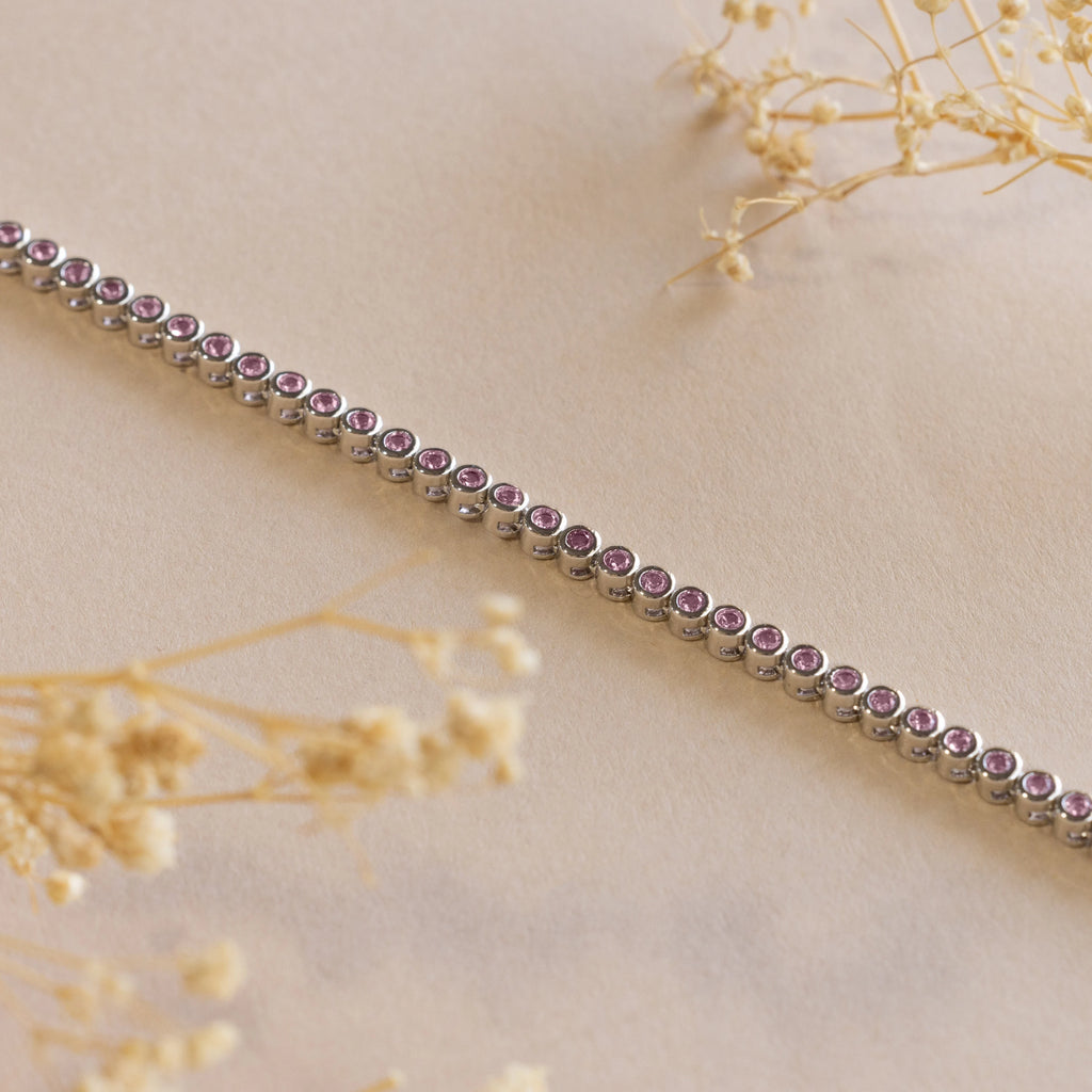 The silver bracelet with small purple gemstones, shown on a beige background with dried flowers, pairs beautifully with the Pink Bezel Tennis Necklace for a coordinated and sophisticated look.