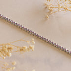 The silver bracelet with small purple gemstones, shown on a beige background with dried flowers, pairs beautifully with the Pink Bezel Tennis Necklace for a coordinated and sophisticated look.