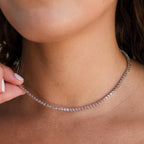 A close-up of a woman wearing the Pink Bezel Tennis Necklace, a delicate silver chain accented with sparkling pink gemstones.