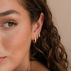 A woman with wavy brown hair wears three elegant gold hoop earrings, including the Opal Inlay Diamond Huggies, on her ear.