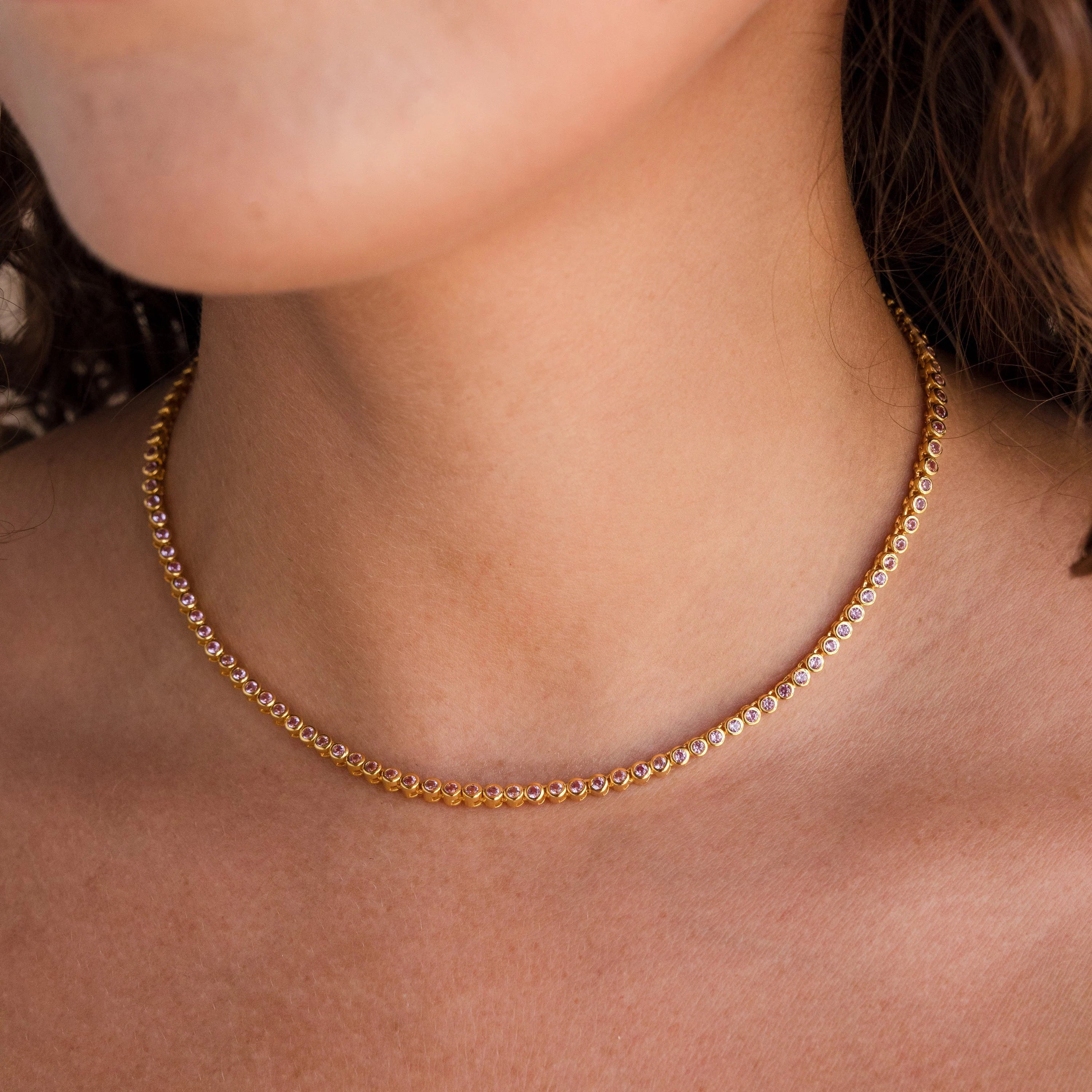 The Pink Bezel Tennis Necklace features small diamonds and delicate pink gemstones in a gold setting, creating an elegant look with a subtle touch of color perfect for any woman's neck.