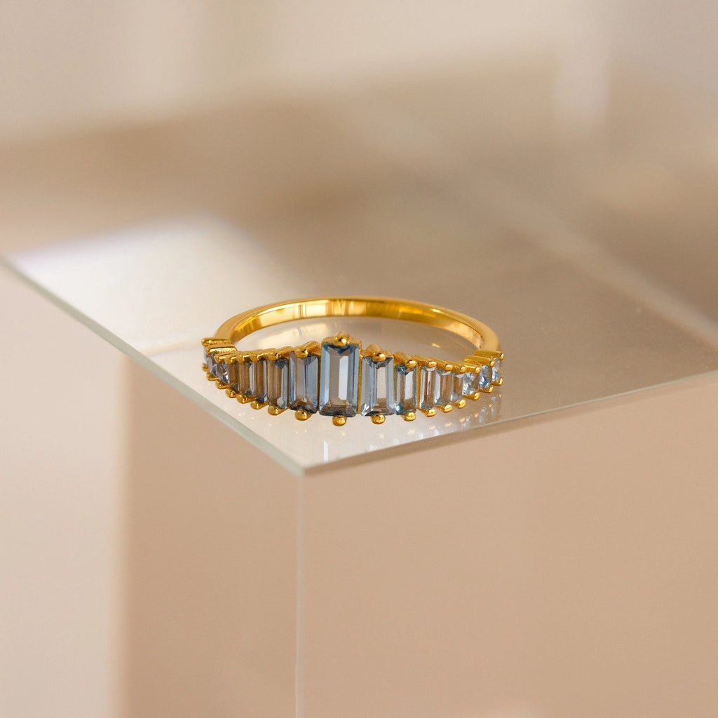 The Art Deco Aquamarine Ring features rectangular, light blue gemstones and is displayed on a clear surface, radiating vintage glamour.