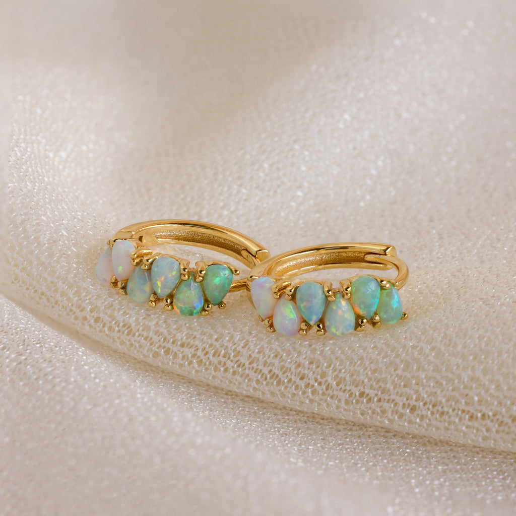 Ombre Opal Huggies displayed on textured cream fabric, these gold hoop earrings feature iridescent opal stones that add subtle shimmer to any look.