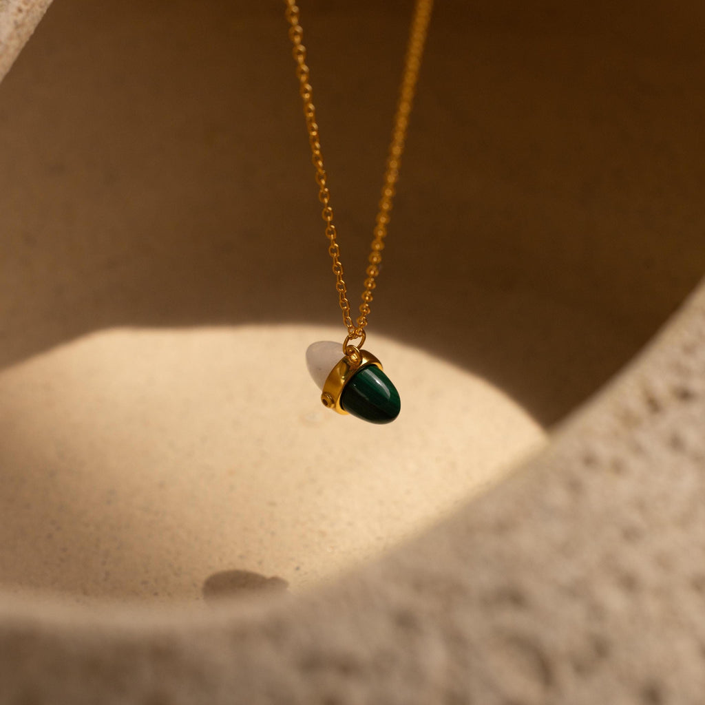 Malachite & Moonstone Necklace featuring a delicate green stone pendant, elegantly set against a textured beige background in soft light—a stunning piece that captures the essence of healing gemstone jewelry.