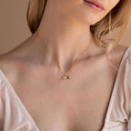A woman in a cream blouse with a low neckline wears the Malachite & Moonstone Necklace, featuring a small round pendant that radiates the subtle elegance of healing gemstone jewelry.