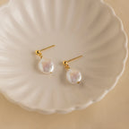 Round Pearl Drop Earrings featuring gold studs and iridescent round baroque pearls displayed on a white scalloped dish—an elegant accessory that brings timeless charm to any look.