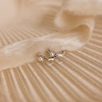 Tiny Pearl Huggies, featuring a delicate pearl accent, are displayed on a soft, cream-colored textured fabric background.