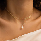 Close-up of a woman wearing the Duo Chain Pearl Necklace, featuring gold chains in layered styles and a delicate strand with a single pearl pendant against bare skin.