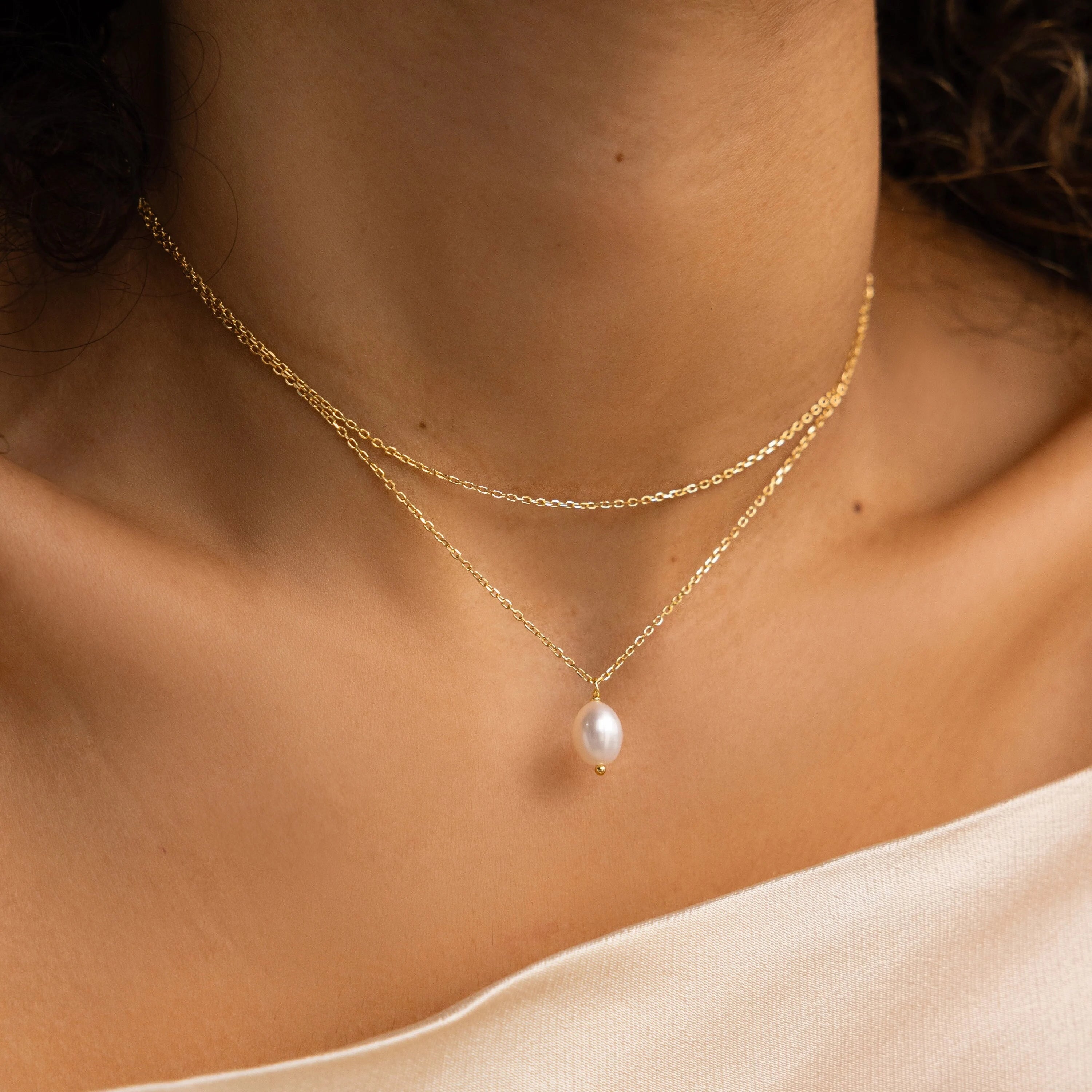 Close-up of a woman wearing the Duo Chain Pearl Necklace, featuring gold chains in layered styles and a delicate strand with a single pearl pendant against bare skin.