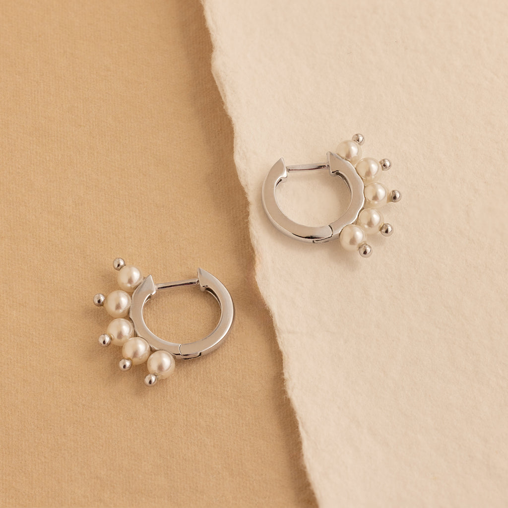 Two Beaded Pearl Huggies featuring clusters of small pearls are displayed on beige textured paper—a refined, modern take on pearl jewelry.