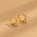Beaded Pearl Huggies—gold hoop earrings with delicate white pearls—capture modern pearl jewelry style, shown here on a beige surface.