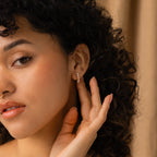 Woman with curly hair touching Beaded Pearl Huggies, elegantly displaying modern pearl jewelry against a soft, neutral background.