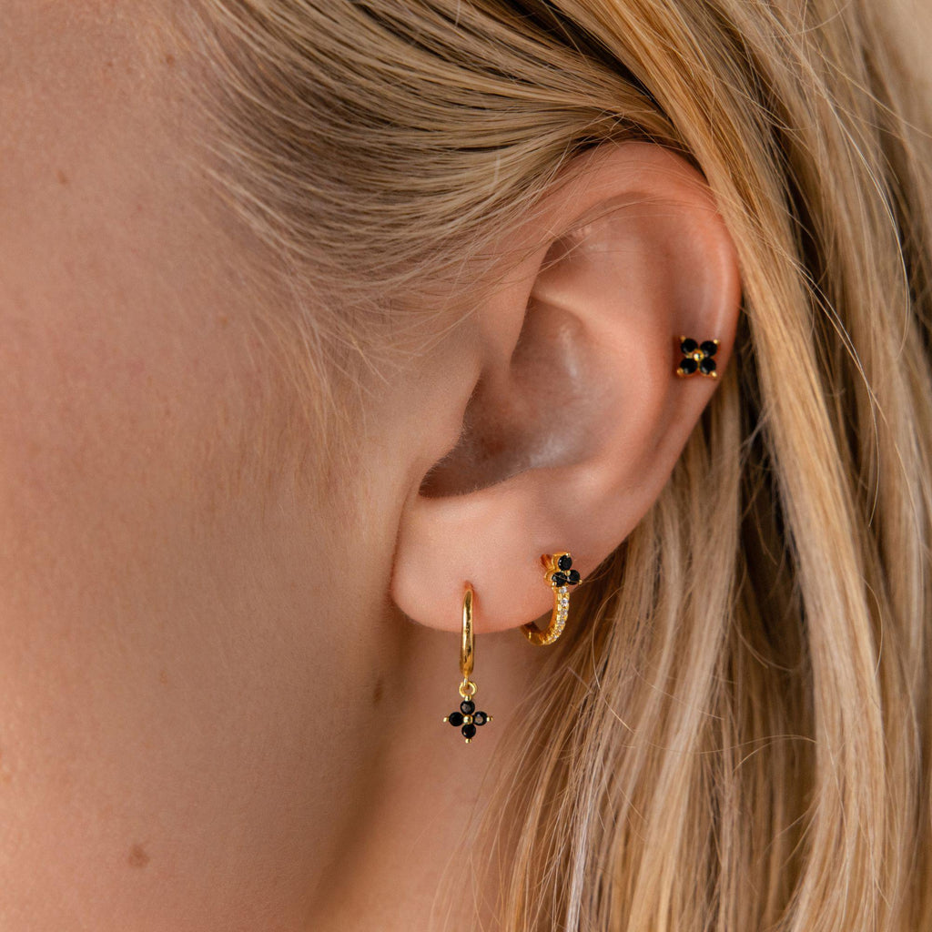 Close-up of an ear with three piercings, each featuring dainty hoops and black onyx jewelry such as the Onyx Lily Huggies.