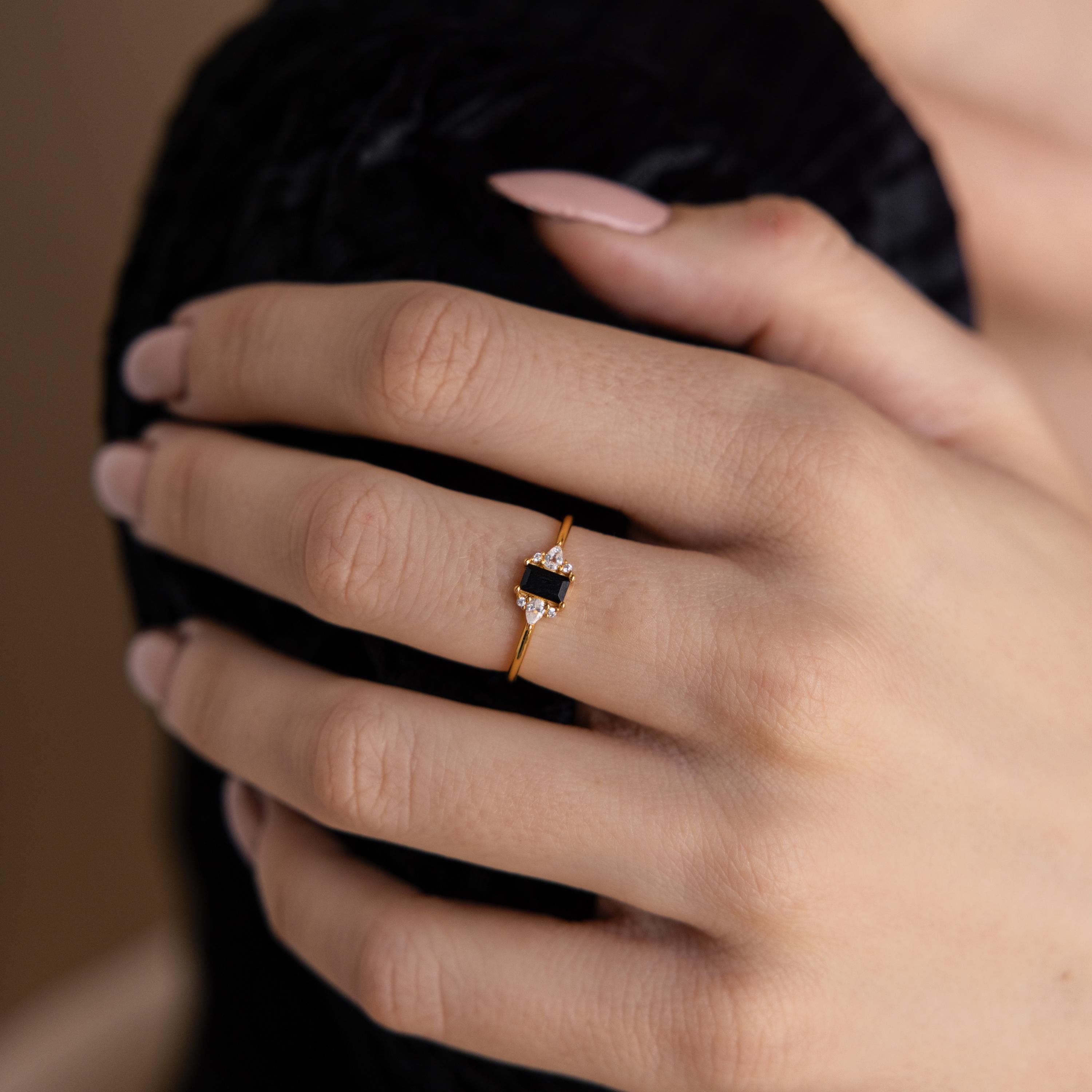 Close-up of a manicured hand wearing the Black Baguette Diamond Ring, a vintage-style gold ring with a striking black and white stone design.
