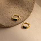 Two Onyx Link Huggies, featuring gold chain hoops with black onyx gemstones, rest on a textured beige surface.