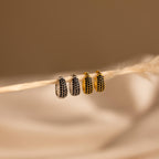 Two pairs of hoop earrings, including modern hoops and the Chunky Onyx Pave Huggies, hang on a string against a soft beige background. One pair is silver, while the Chunky Onyx Pave Huggies shine in gold.