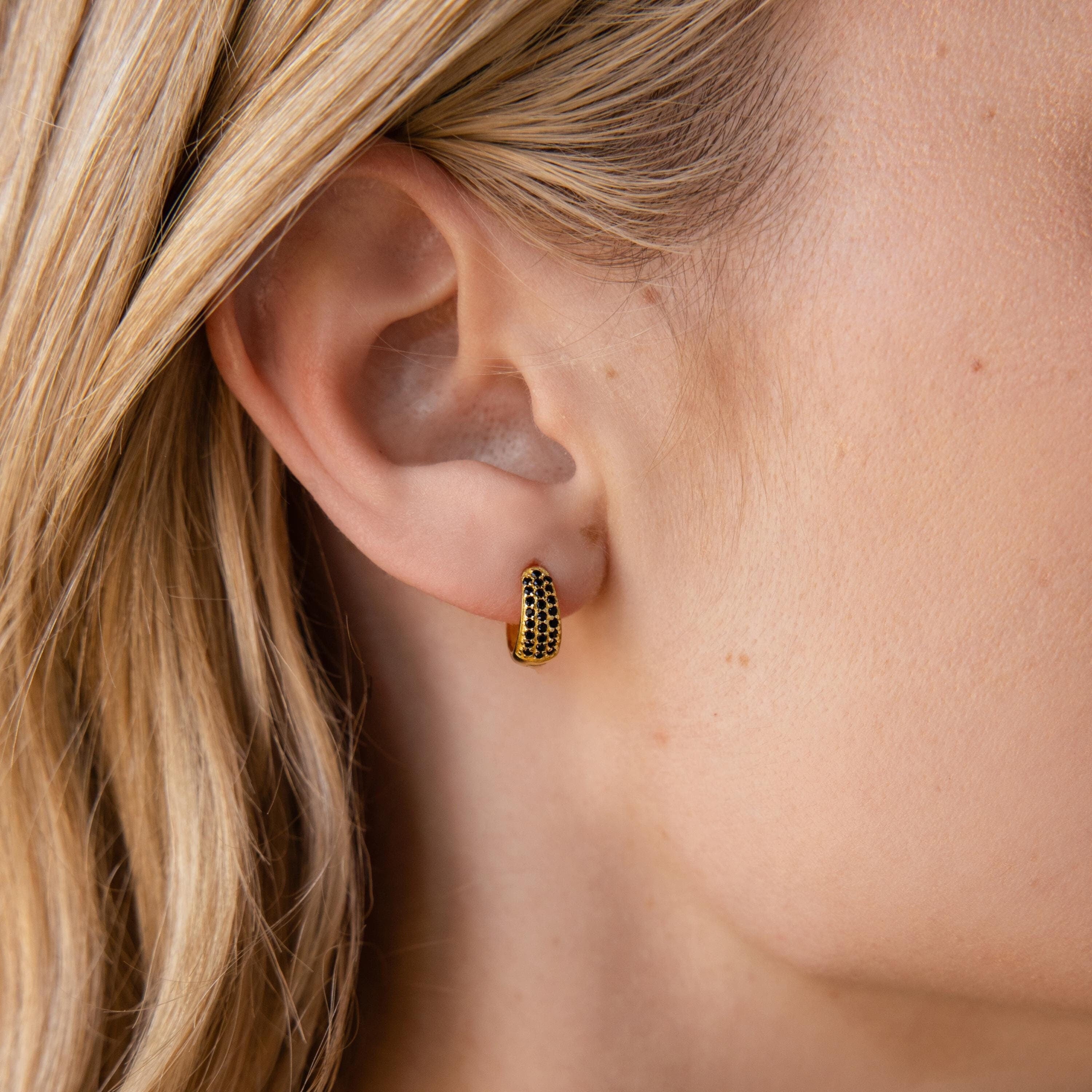 A close-up of a woman's ear wearing Chunky Onyx Pave Huggies.