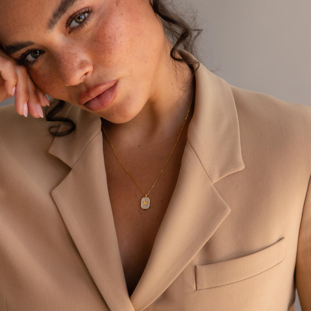 Woman in beige blazer with wavy hair, wearing a Pave Pearl Initial Necklace and looking into the camera.