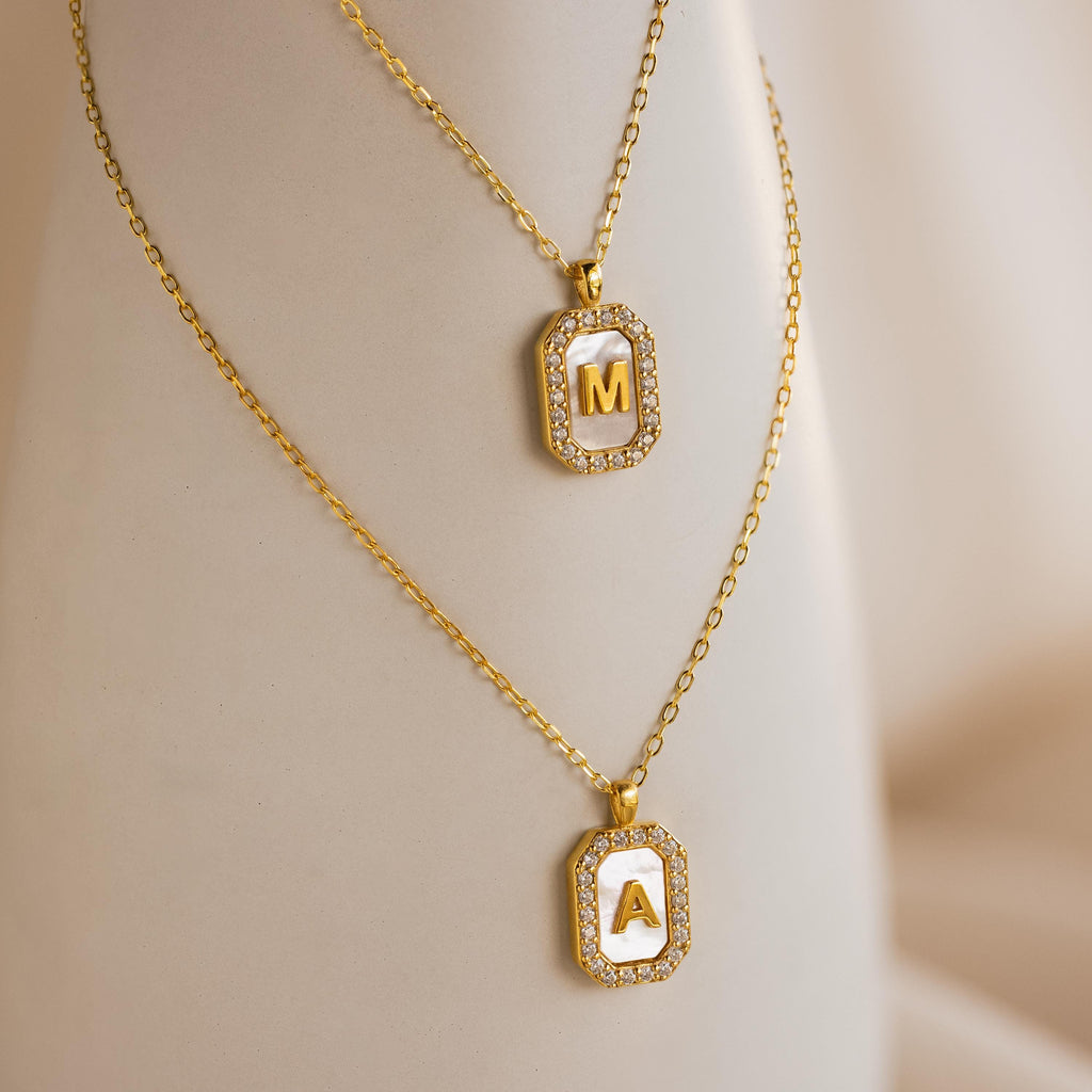 Two Pave Pearl Initial Necklaces in gold, each with a rectangular pendant bordered by sparkling CZ diamonds and personalized with the letters M and A.