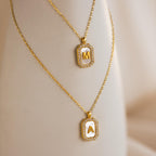 Two Pave Pearl Initial Necklaces in gold, each with a rectangular pendant bordered by sparkling CZ diamonds and personalized with the letters M and A.