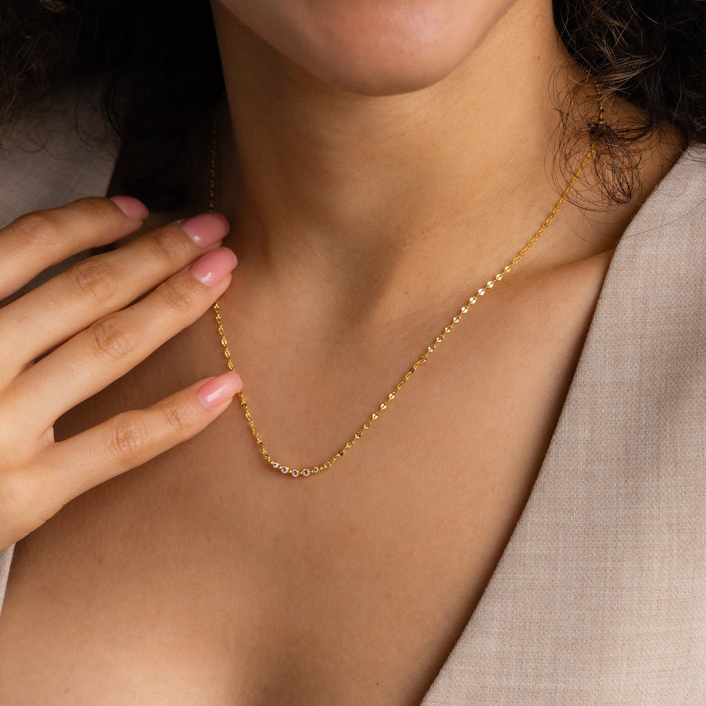 Close-up of a woman wearing the Lace Birthstone Necklace, her hand gently touching her collarbone, styled with a beige blazer.