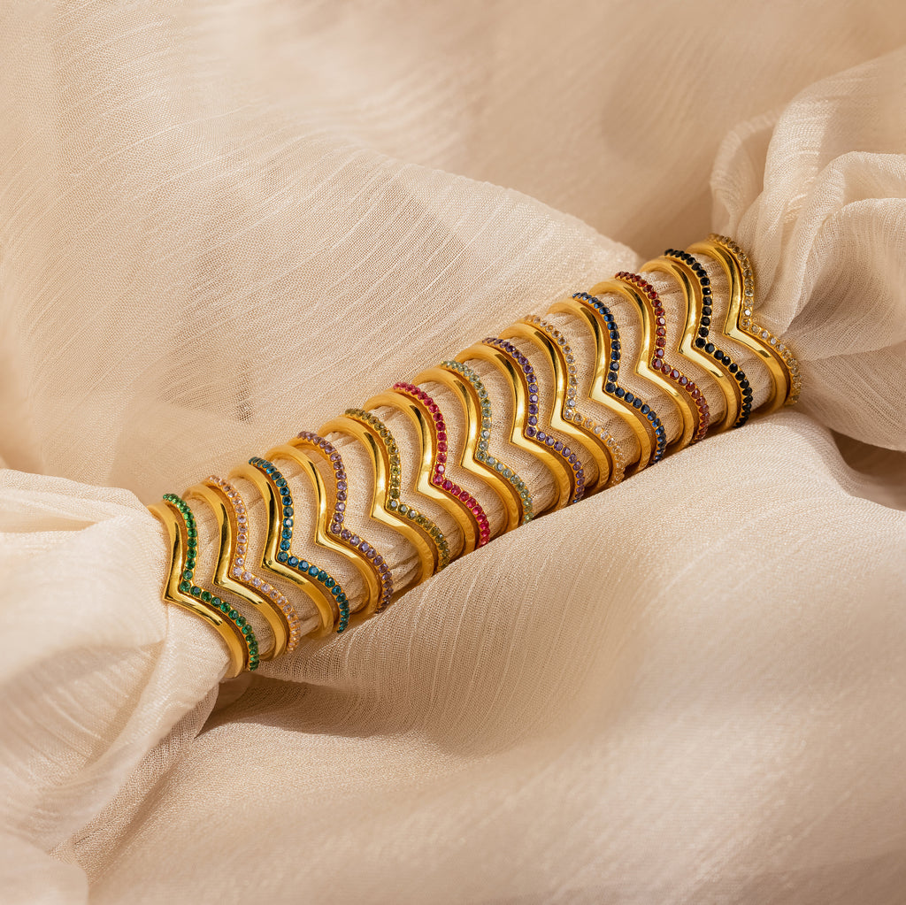 The Chevron Birthstone Rings Set features vibrant, wavy chevron patterns and is displayed on cream-colored fabric.