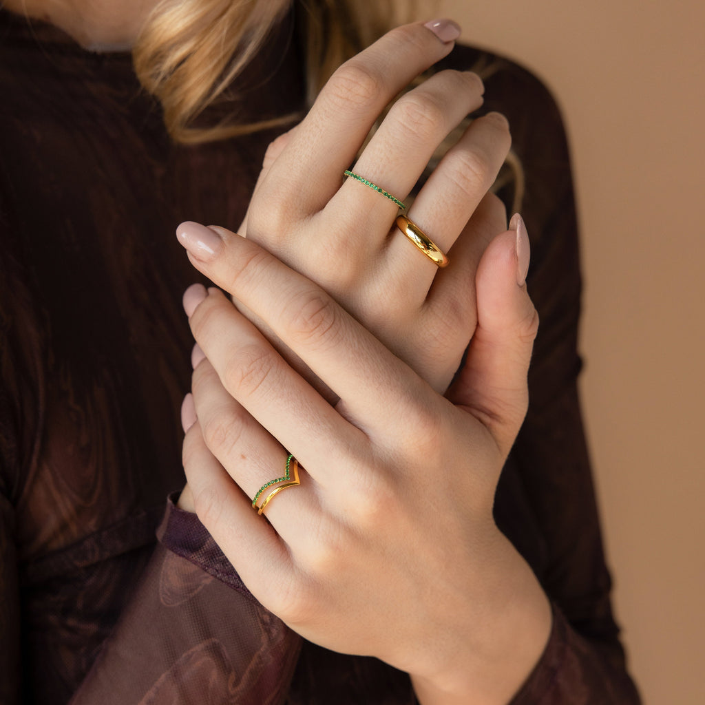 A woman with manicured nails gently clasps her hands, showcasing three gold rings from the Chevron Birthstone Rings Set on her fingers.