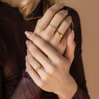 A woman with manicured nails gently clasps her hands, showcasing three gold rings from the Chevron Birthstone Rings Set on her fingers.