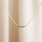 The Lace Birthstone Necklace features a gold chain with five small green beads, shown on a neutral light background—a delicate birthstone necklace ideal for everyday elegance.