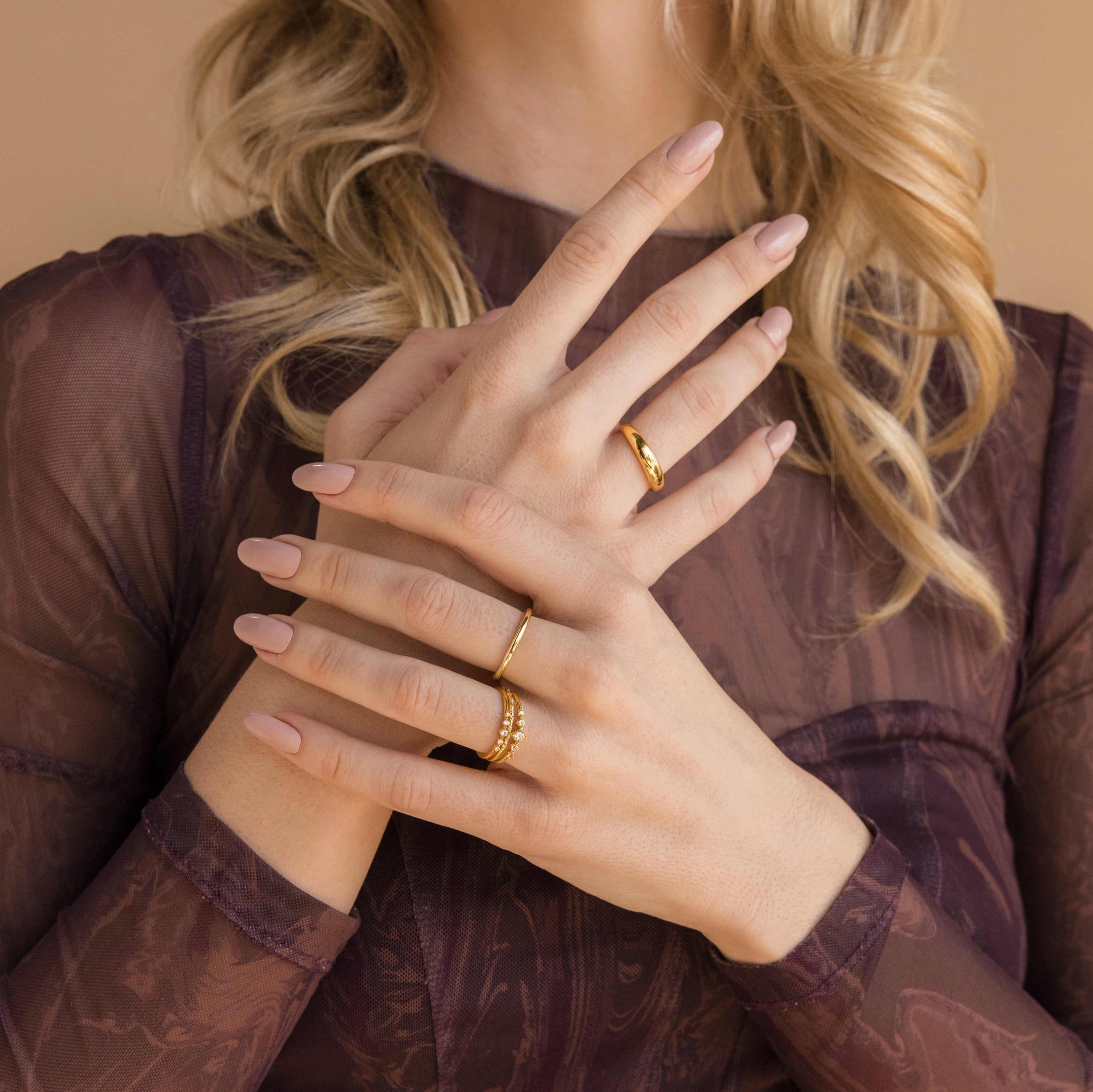A blonde woman wears the Lace Birthstone Rings Set, styling the minimalist rings on her hands crossed elegantly over a sheer purple top.