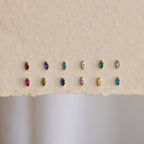 Twelve pairs of Marquise Birthstone Studs, each with colorful personalized gemstones in gold settings, are displayed on textured paper.